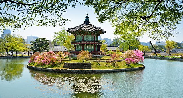 Petit pavillon coréen traditionnel au centre d’un étang, entouré de fleurs printanières et d’arbres verdoyants, sous un ciel clairverdoyants, sous un ciel clair